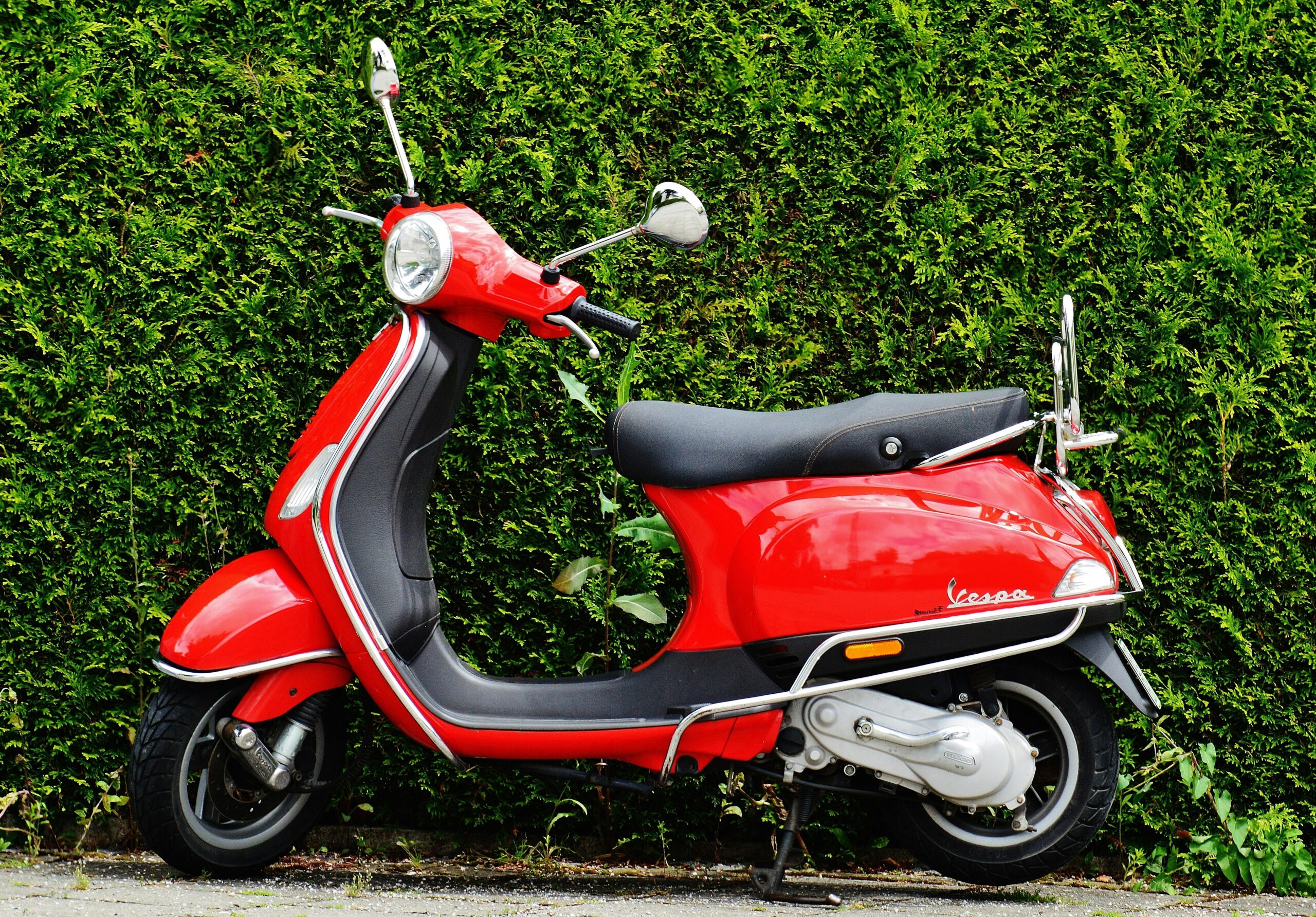 Bright red Vespa scooter parked against a lush green hedge, showcasing vibrant contrast.